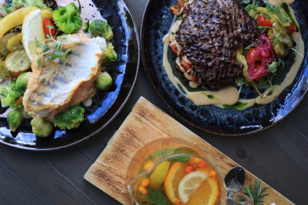 Top view of gourmet fish and steak dishes with fresh citrus and herbs on a stylish table setting.